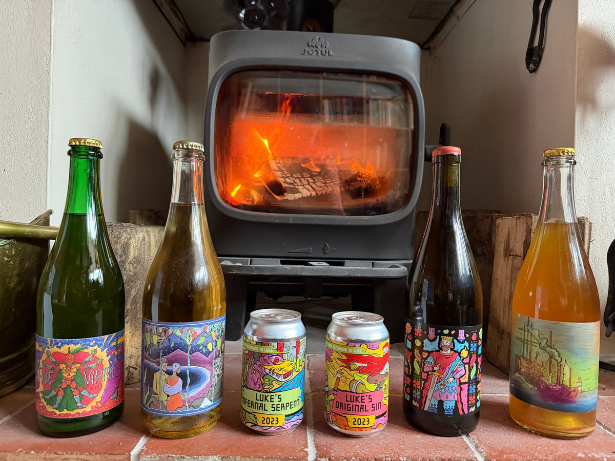 Luke's Cider bottles and cans in front of a wood stove, as featured in Cider Review